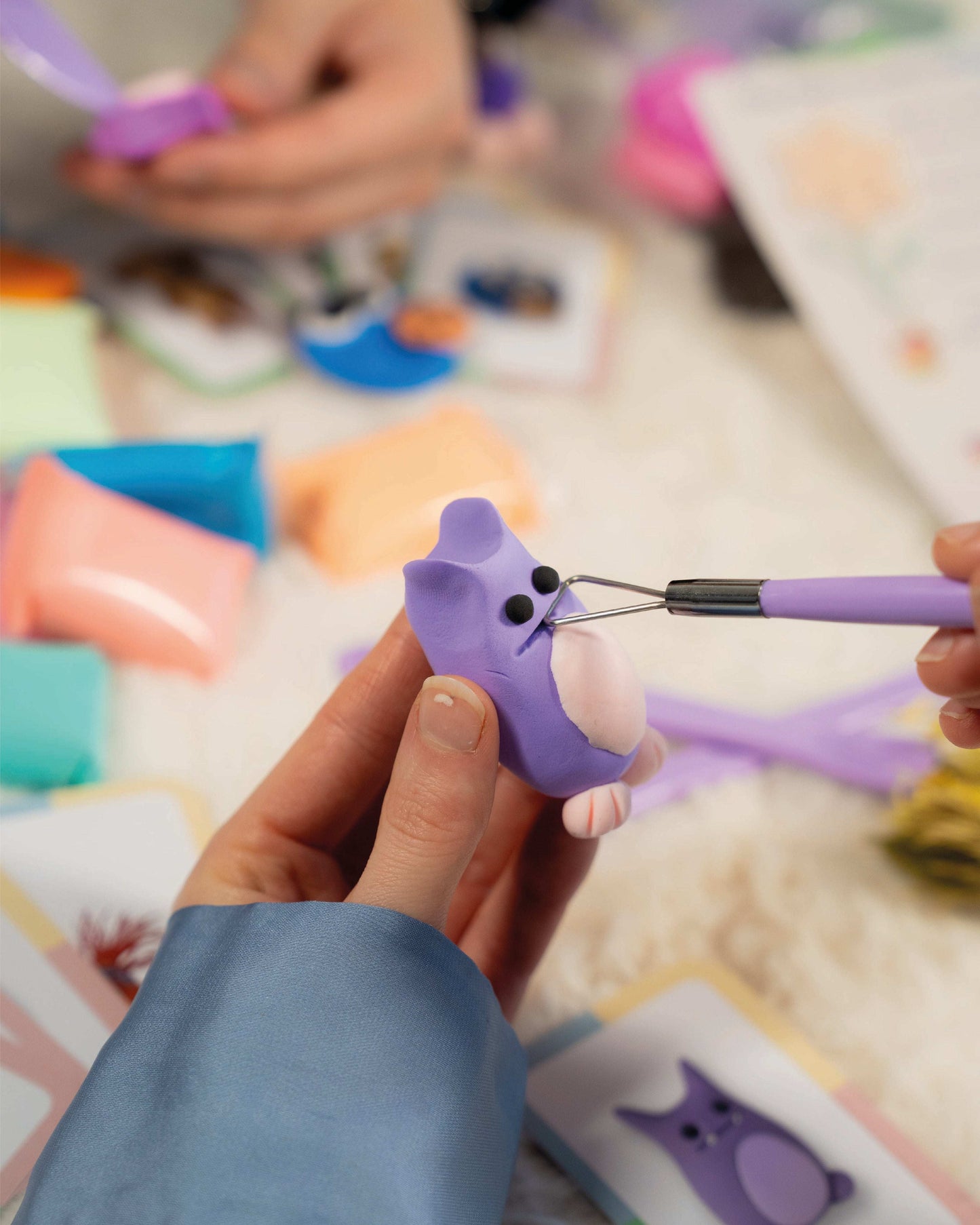 Person using a tool to shape a purple plastic animal figure on a colorful surface with Extra Sculpting Tools