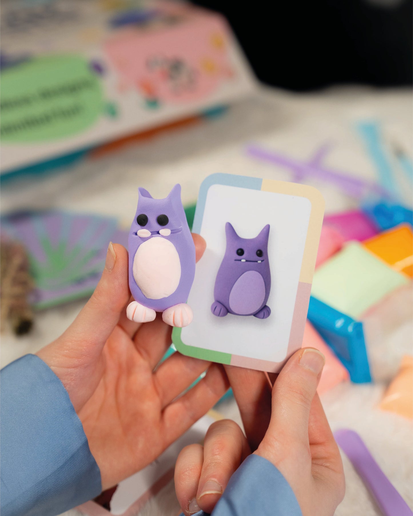 Two purple cartoon-like figures held by hands with colorful objects in the background