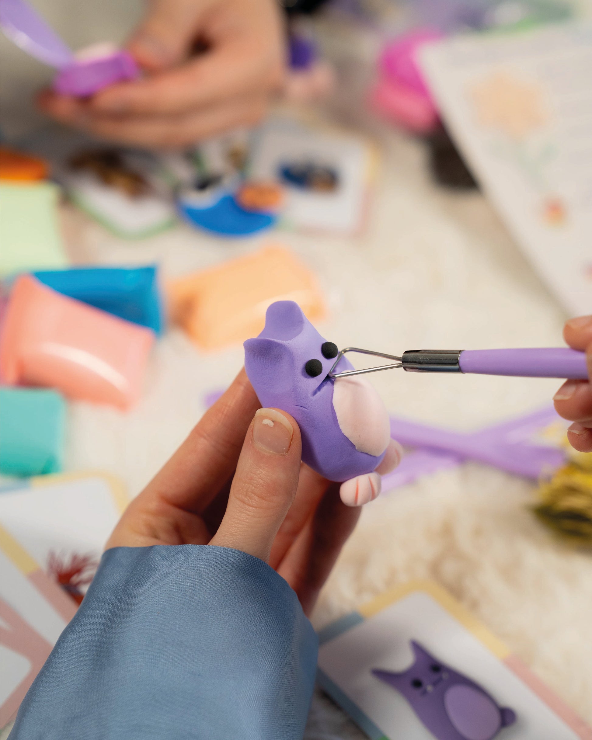 Person using a tool to shape a purple plastic animal figure on a colorful surface.