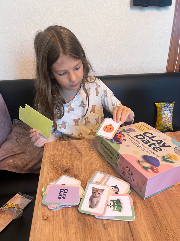 Child playing with 'Clay Date' game cards on a wooden table.