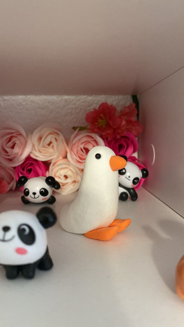 Decorative setup with a white duck, panda figures, and pink flowers on a shelf.
