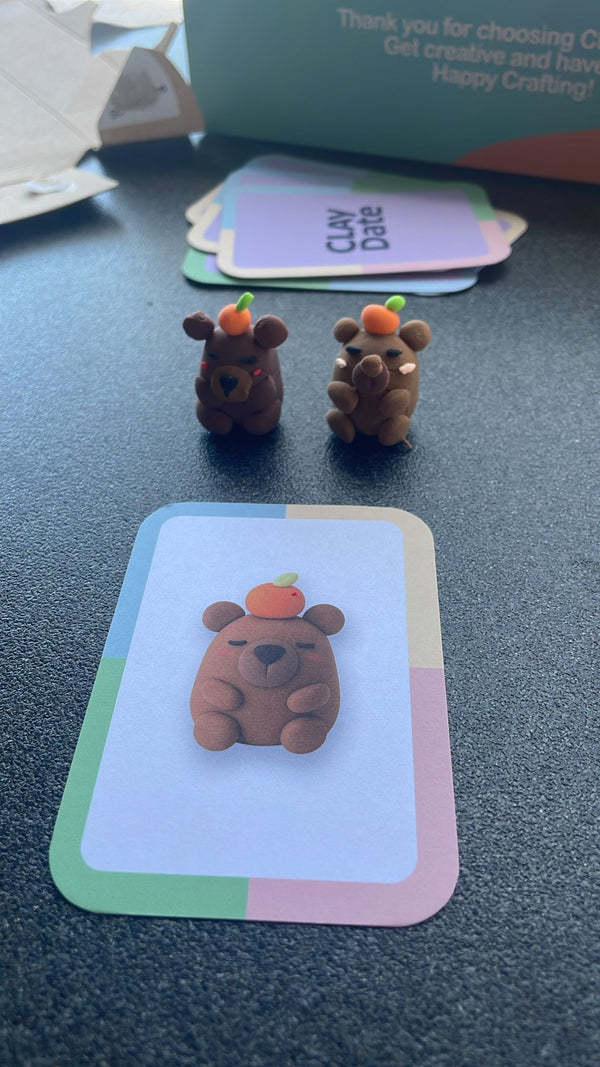 Two small brown bear figurines with orange hats on a card with a bear design.