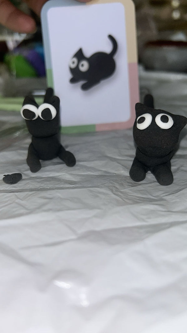 Two black cat figurines with googly eyes on a marble surface.