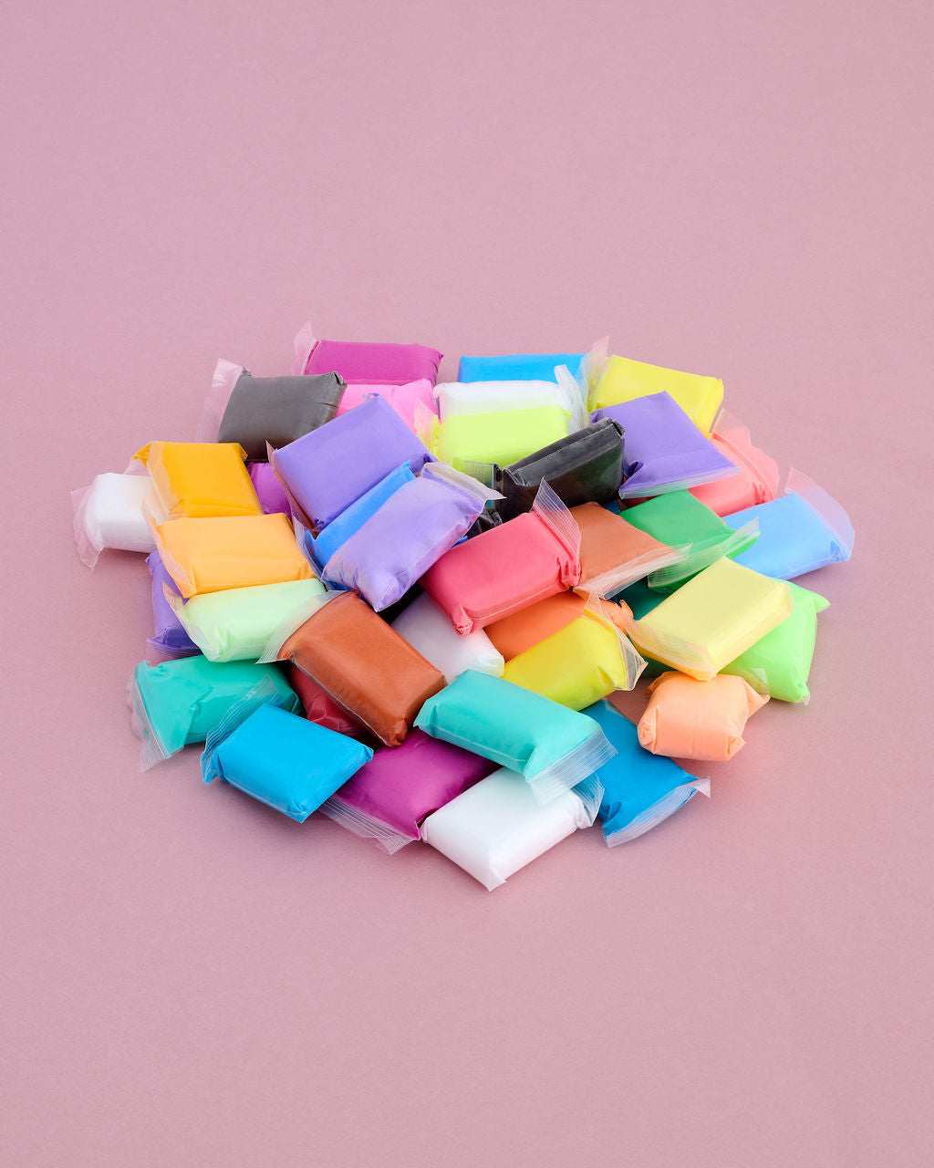 A pile of colorful, individually wrapped clay or modeling compound pieces on a solid pink background.