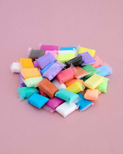 A pile of colorful, individually wrapped clay or modeling compound pieces on a solid pink background.