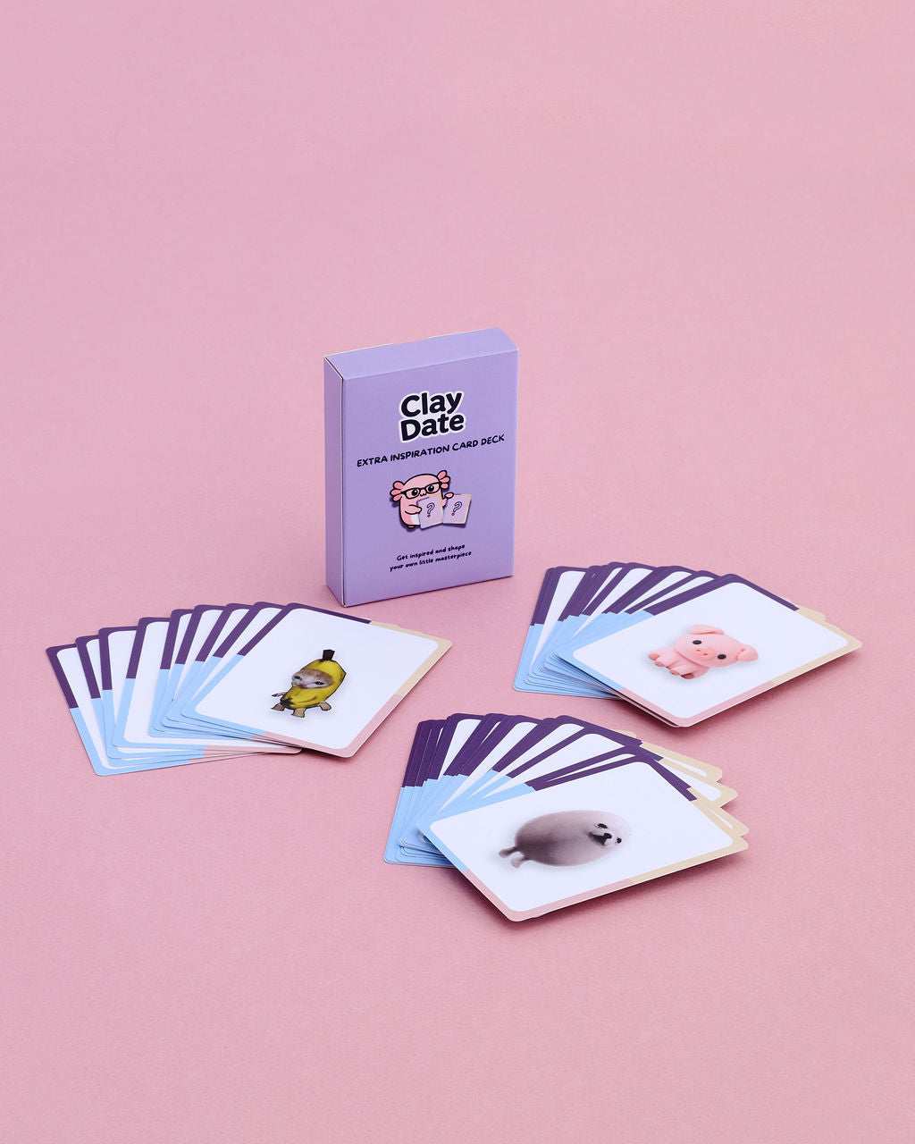 A boxed card game called Clay Date stands upright on a pink background, with several illustrated cards fanned out in front. 