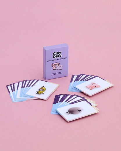 A boxed card game called Clay Date stands upright on a pink background, with several illustrated cards fanned out in front. 