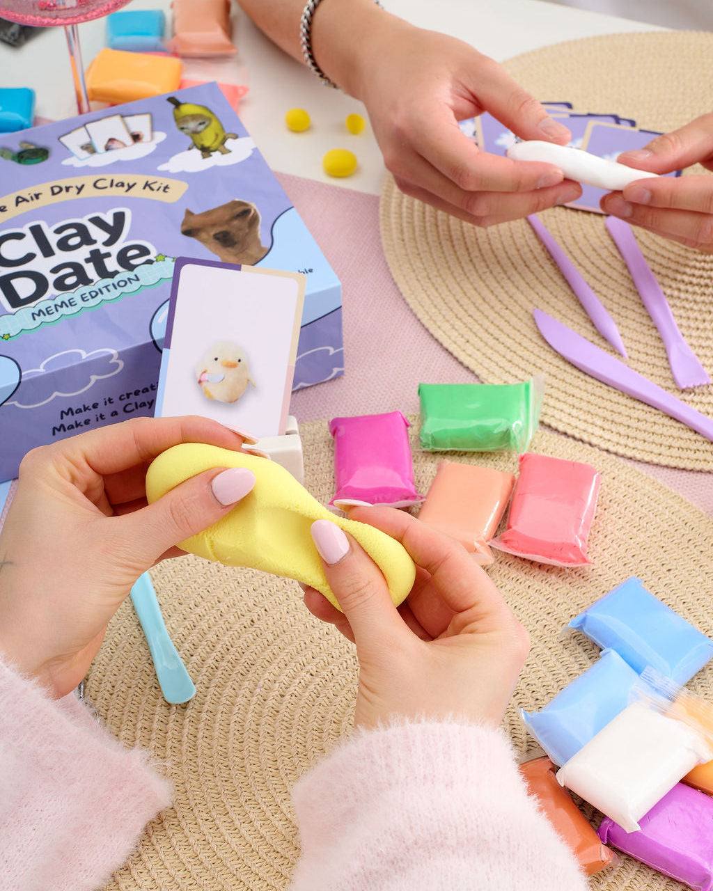 Hand shaping clay next to meme cards from the Clay Date™ Meme Kit