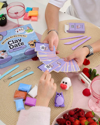 A clay craft kit set up on a table with hands assembling or playing with the kit. 