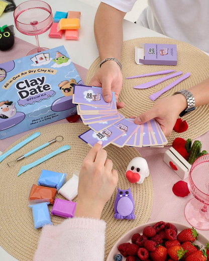 A clay craft kit set up on a table with hands assembling or playing with the kit. 
