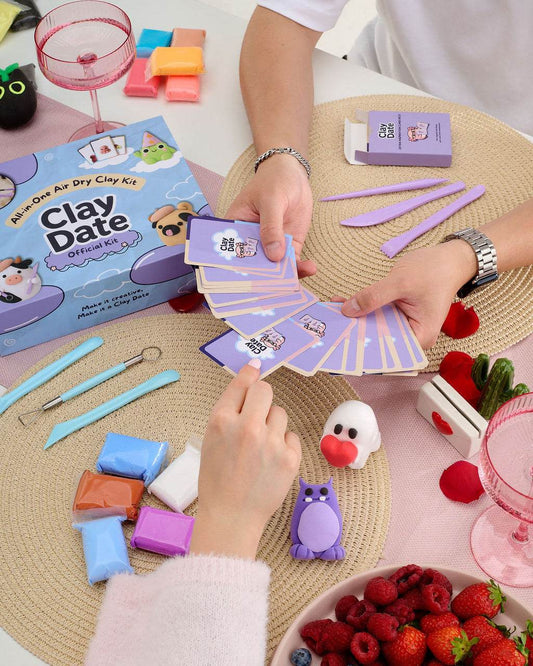 A clay craft kit set up on a table with hands assembling or playing with the kit. 
