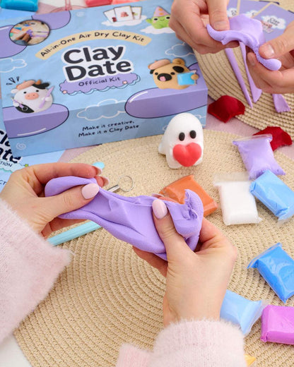 A person's hands stretching a purple clay figure over a woven beige mat, with a blue and purple 'Clay Date Official Kit' box.