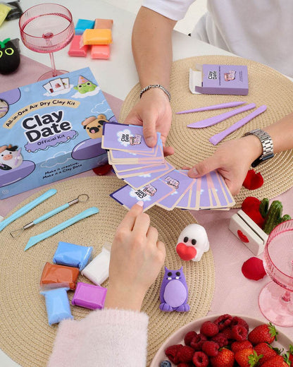 Person holding inspiration cards and clay pieces next to the Clay Date New Official Kit box