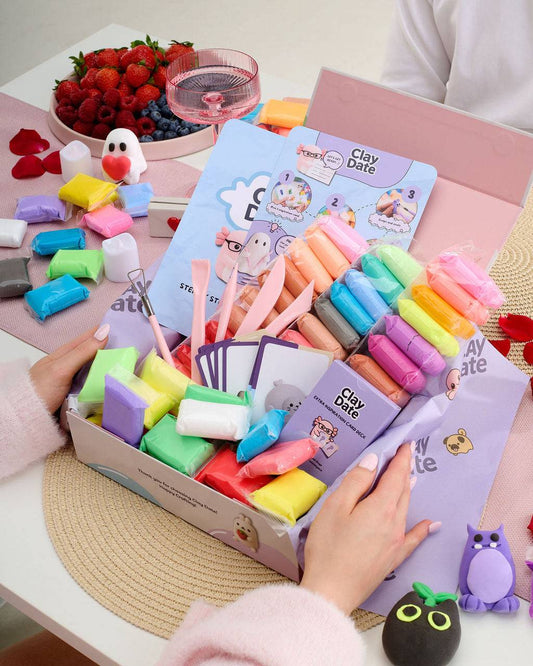 A colorful clay art kit displayed in an open box on a table, with hands holding the packaging. 